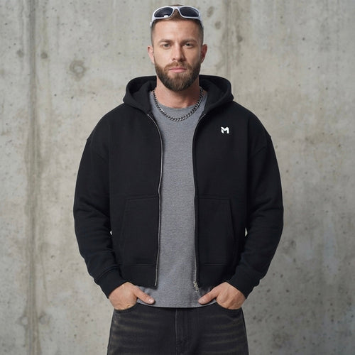 MINIMAL black fleece full zip-up hoodie with logo on chest worn by a bearded man against a concrete background